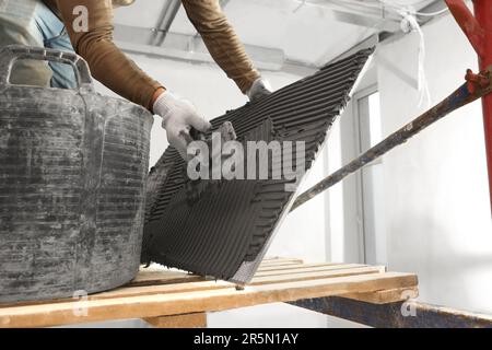 Lavoratore che applica cemento su tegola per l'installazione in stanza, primo piano Foto Stock