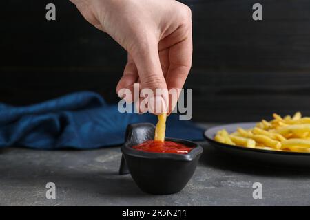 Donna che immerga la frittura francese in ketchup al tavolo grigio, primo piano Foto Stock