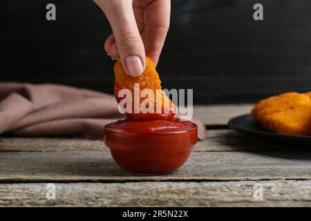 Donna che tuffa il nocciolo delizioso del pollo in ketchup al tavolo di legno, primo piano Foto Stock