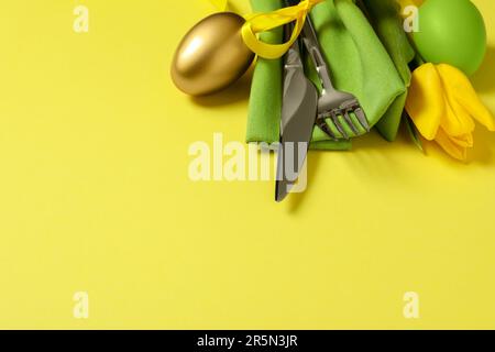 Set di posate, uova dipinte e bel fiore su sfondo giallo, spazio per il testo. Festa di Pasqua Foto Stock