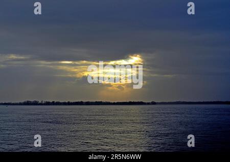 Tempesta sul fiume. Nuvole pesanti sull'acqua, un fascio luminoso di luce separa le nuvole. Luce del sole sulle nuvole. Increspature sulla superficie dell'acqua. Pioggia accesa Foto Stock