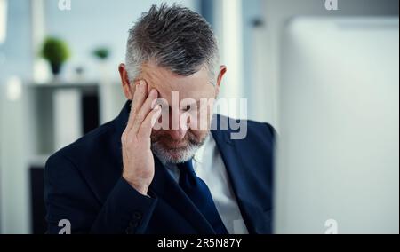 La tensione è in ingresso. un uomo d'affari maturo che avverte un mal di testa mentre lavora alla sua scrivania in un ufficio moderno. Foto Stock