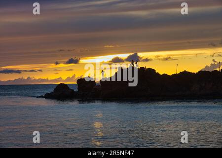 I tuffatori della scogliera si preparano per tuffarsi alla roccia nera a Maui al tramonto. Foto Stock