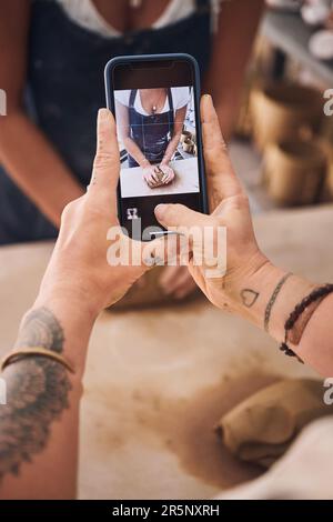 I ricordi si trasformano in ogni pezzo realizzato. una donna che usa uno smartphone per scattare foto della sua amica in uno studio di ceramica. Foto Stock