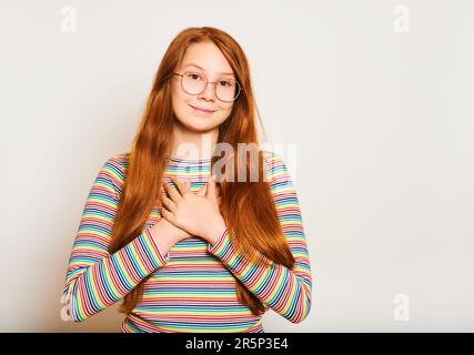 Studio ritratto di ragazza thankfull giovane con felice espressione facciale, tenendo le mani sul petto Foto Stock