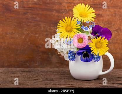 piccolo bouquet primaverile. Bouquet di fiori selvatici in un piccolo vaso su un tavolo di legno. Bouquet di margherite. Foto Stock