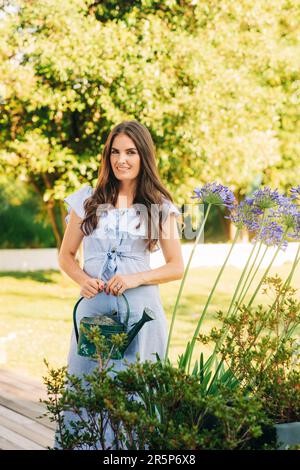 Bella giovane donna che innaffia le piante nel giardino estivo Foto Stock