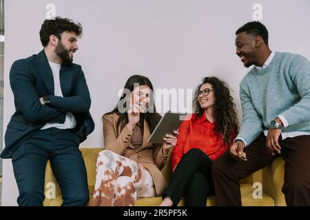 Quattro uomini d'affari sorridono mentre si siedono sul divano giallo del posto d'affari Foto Stock