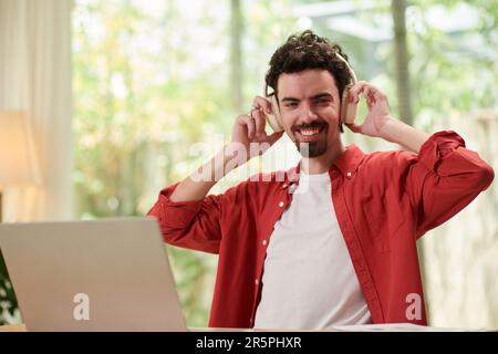 Ritratto di un uomo allegro che ascolta podcast o audiolibri quando lavora su un computer portatile Foto Stock