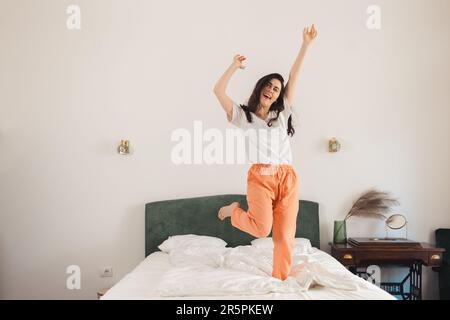 Felice giovane donna caucasica danze a letto in camera da letto. Libertà e vincita. Foto Stock