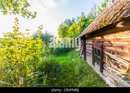 Un vecchio bagno nel villaggio. Edificio in legno con luce del tramonto. Foto Stock