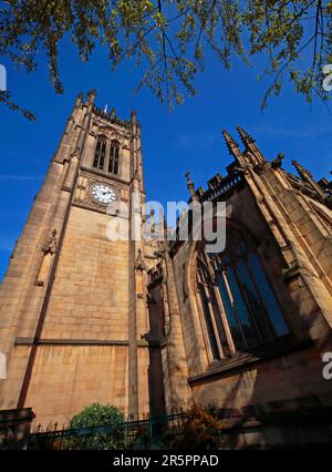 La torre dell'orologio della Cattedrale di Manchester fotografata in estate sotto un cielo azzurro e limpido, evidenziando l'architettura gotica in pietra del centro storico della città Foto Stock