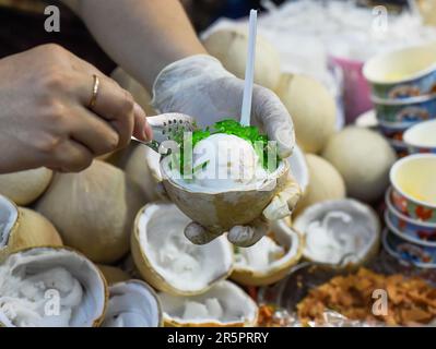 Mani che servono gelato bianco in cocco nel mercato notturno vietnamita e festival alimentare Foto Stock