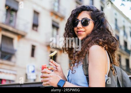 giovane viaggiatore turco con zaino e occhiali da sole con una tazza di frutta fresca per strada Foto Stock