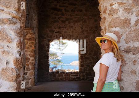 turista vecchia donna sorridente con occhiali da sole guardando a tossa de mar con un cappello. In viaggio d'estate. Vista posteriore Foto Stock
