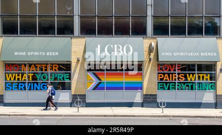 Toronto, Canada - 4 giugno 2023: Due persone che camminano su un marciapiede da Pride arcobaleno simboli di colore in un negozio LCBO nel quartiere del centro. Tradizionale Foto Stock