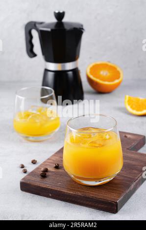 Succo d'arancia con ghiaccio su sfondo grigio, preparazione di una bevanda rinfrescante al caffè, due bicchieri di succo d'arancia fresco Foto Stock