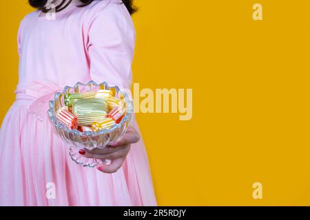 Bambina che tiene in mano una ciotola di cioccolato di lusso avvolto. In piedi su uno sfondo giallo isolato, spazio di copia. Festa religiosa tradizionale dello zucchero Foto Stock