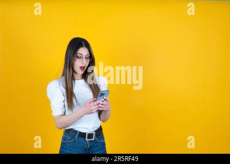 donna scioccata. Sorpresa caucasica ragazza tenere e utilizzare lo smartphone. Navigare nei social media, leggere un messaggio, espressione emotiva del volto della giovane donna Foto Stock