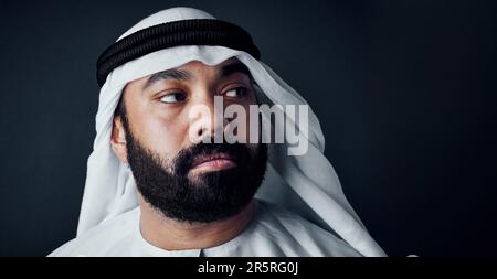 Pensare sempre al business. Studio di un giovane vestito di abiti tradizionali islamici che si posano su uno sfondo scuro. Foto Stock