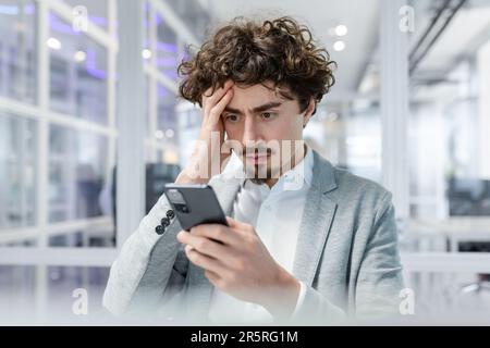 Un uomo d'affari preoccupato tiene il telefono nelle sue mani, guarda. Lettura di cattive notizie, ricevuto un messaggio. Foto Stock