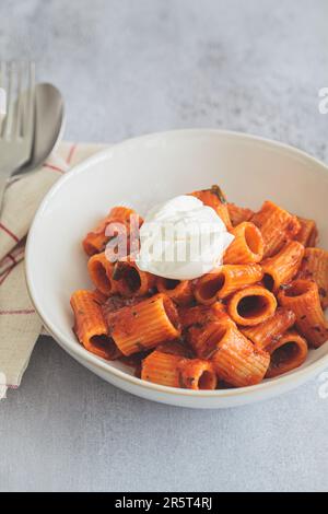 Pasta vegetariana con salsa di pomodoro e formaggio cremoso in una ciotola bianca, sfondo grigio. Foto Stock