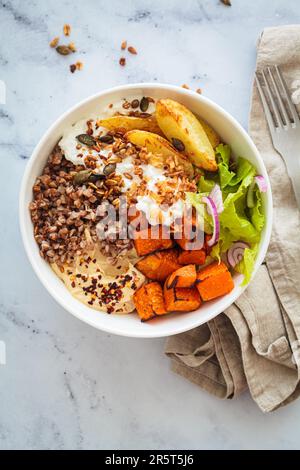 Ciotola vegetariana buddha con grano saraceno, formaggio casolare, hummus e patate dolci al forno, vista dall'alto. Concetto di cibo equilibrato. Foto Stock