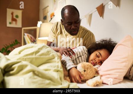 Piccolo figlio che dorme nel suo letto con il giocattolo mentre papà lo mette e gli dice la storia Foto Stock