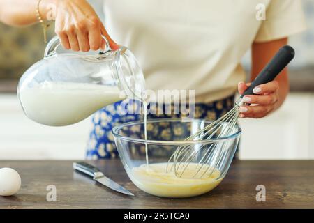 La mano di primo piano aggiunge latte all'impasto per la frittella. Ingredienti per focaccia, torta, pizza, ravioli, pasta. panetteria, libro di cucina, blog di cucina. Foto Stock