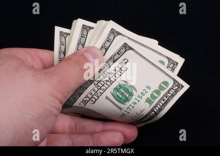 Un maschio caucasico in una camicia bianca che tiene una pila di banconote da cento dollari nella loro mano destra Foto Stock