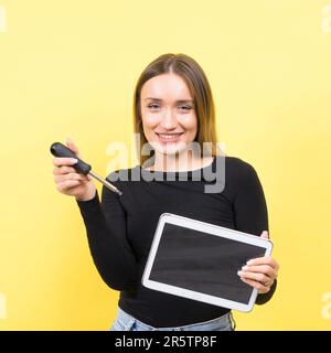 Centro servizi. Riparazione del notebook. Il cacciavite femmina svita i bulloni del computer portatile su sfondo giallo Foto Stock