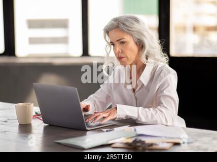 Seria e matura Businesswoman che utilizza il notebook per lavorare in ufficio indoor Foto Stock