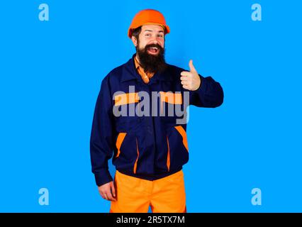 Lavoratore di costruzione o costruttore in abbigliamento da lavoro e l'elmetto che mostra il pollice in su. Riparatore in uniforme e casco di sicurezza. Costruttore o ingegnere in uniforme con o Foto Stock