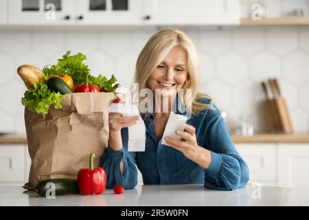 Consegna sul mercato. Donna matura felice che verifica le fatture in cucina dopo l'acquisto della drogheria Foto Stock