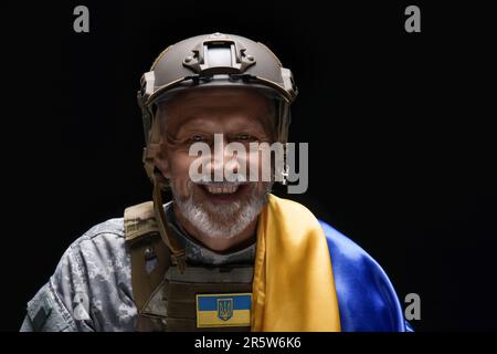 Buon soldato maturo con bandiera Ucraina su sfondo nero, primo piano Foto Stock