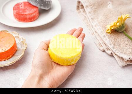 Mano femmina con shampoo solido fatto a mano e fiore di calendula su sfondo chiaro, primo piano Foto Stock