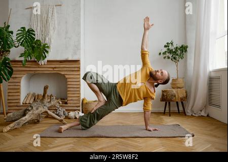 L'uomo che pratica lo yoga in piedi a mano posa nel salotto di casa Foto Stock