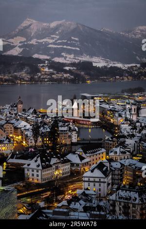 Una vista verticale aerea di edifici illuminati vicino all'acqua e una maestosa catena montuosa a Lucerna, Svizzera Foto Stock