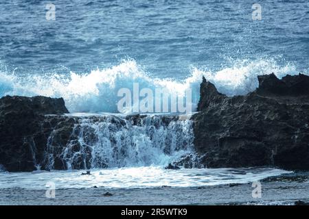 Una grande onda si schianta contro la costa rocciosa di un corpo d'acqua, creando una scena drammatica Foto Stock