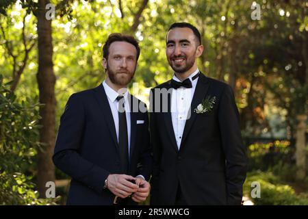 Lo sposo e l'uomo migliore nei vestiti che posano davanti ad uno sfondo verde blurry Foto Stock