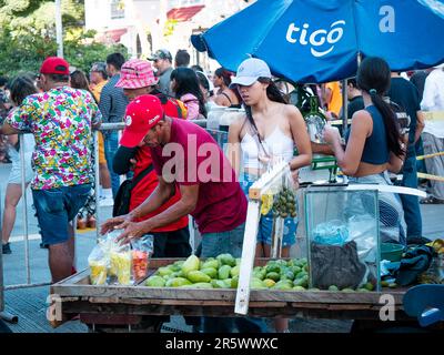 Barranquilla, Atlantico, Colombia - Febbraio 21 2023: Giovane donna colombiana che acquista frutta in una tazza di plastica da un venditore di strada Foto Stock