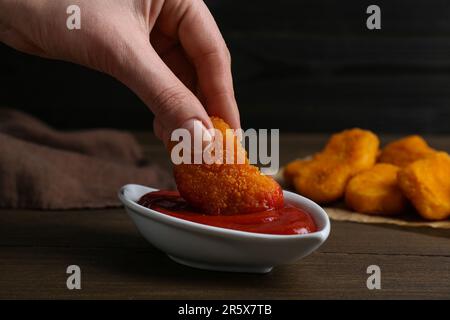 Donna che tuffa il nocciolo delizioso del pollo in ketchup al tavolo di legno, primo piano Foto Stock