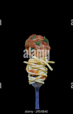 Spaghetti tubolari, polpette e salsa di pomodoro lucenti e succosi su forchetta verticale, su fondo nero al centro della cornice con spazio copia Foto Stock