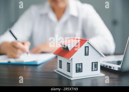 Gli agenti immobiliari offrono contratti per l'acquisto o l'affitto residenziale. La persona di affari le mani con il modello domestico, la piccola casa rossa dell'edificio. Proprietà ipotecaria Foto Stock