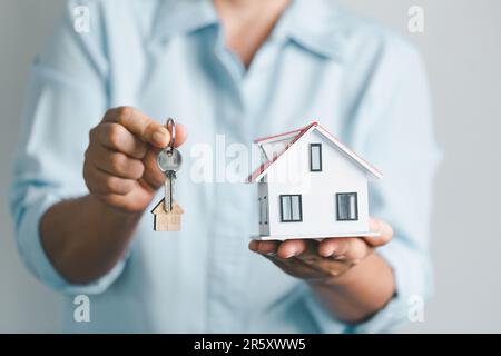 chiave alla vostra propria sede nel palmo della ragazza e un legno per la proprietà di affitto del bene immobile. Modello di casa e chiave in casa porta. Offerta agente immobiliare Foto Stock