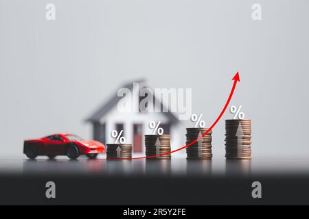 Pile di monete e modello di casa e auto con simbolo percentuale per aumentare i tassi di interesse. Tassi di interesse finanziari e ipotecari. Icona percentuale Foto Stock