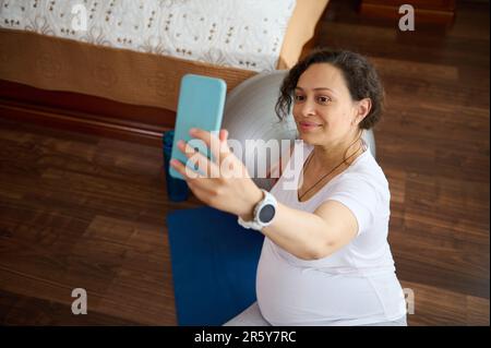 Primo piano donna incinta fa selfie, si rilassa dopo esercizi di stretching per mantenere il corpo in forma in gravidanza Foto Stock