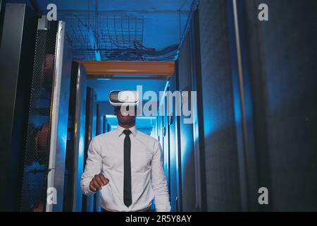 Vivere la vita dei server anche con la simulazione. Un giovane specialista IT che si trova da solo nella sala server e indossa una cuffia per la realtà virtuale. Foto Stock