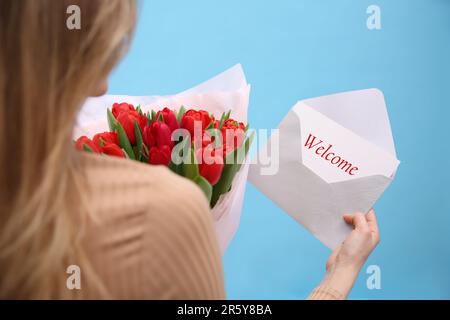 Carta di benvenuto. Donna che tiene busta e bouquet di tulipani rossi su sfondo azzurro, primo piano Foto Stock