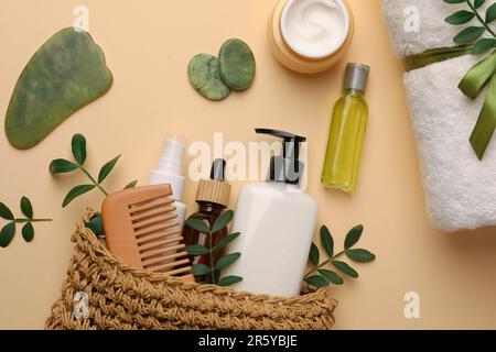 Borsa da bagno compatta con diversi prodotti cosmetici, pietre spa e asciugamano su sfondo beige, piatto Foto Stock